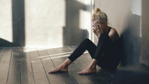 woman sitting alone on the floor covering her face representing anxious attachment after a breakup
