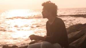 man sitting alone on rocks at sunset reflecting on self-worth and anxious attachment