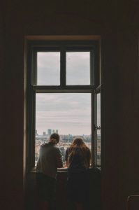 couple sitting together at a dark window overlooking a city representing situationship anxiety and undefined relationships
