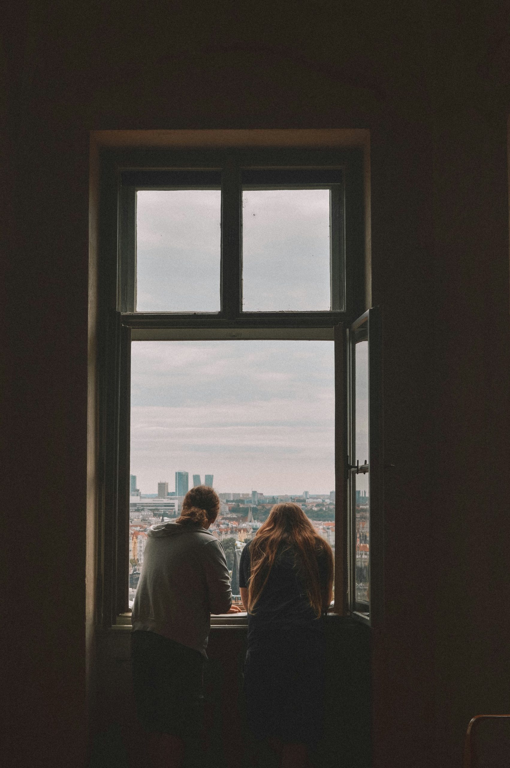 couple sitting together at a dark window overlooking a city representing situationship anxiety and undefined relationships