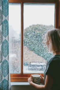 woman looking out rainy window holding mug reflecting on difficulty receiving words of affirmation